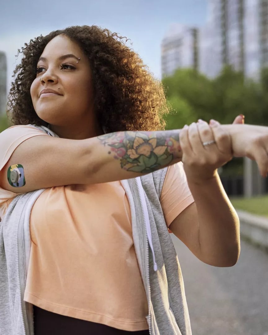 A woman stretching outdoors while wearing a glucose monitor
